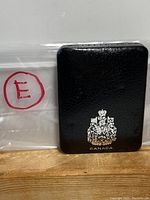 Black leather-like case with Canadian crest and the word 'CANADA' embossed on it. Bag marked with red 'E' included.