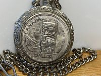 Close-up front view of the silver pocket watch showing the embossed 1958 Canadian silver dollar design with totem pole and mountain scene.