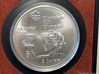Close-up of the reverse side showing Olympic torch, Olympic rings, laurel crown, Montreal 1976, XXI Olympiad, and 5 Dollars denomination