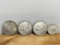 Front view of the four Canadian coins arranged side by side showing the caribou design on the quarters and the smaller dime.