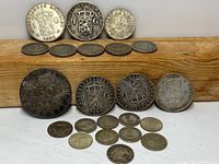 Group of 22 silver coins displayed on wooden surface showing front and back sides of coins