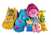 Five Disney Pixar plush toys arranged in a row including Dinoco race car, Sulley, green alien, pink-haired Trolls character, and two yellow monsters