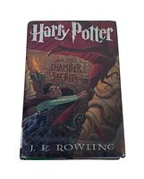 Front cover of the 1st edition hardcover book Harry Potter and the Chamber of Secrets showing Harry on a broomstick with a dark cave background and the title in distinct font.
