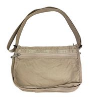 Front view of the small beige crossbody bag showing the front zipper pocket and Lesportsac branding on fabric trimming.