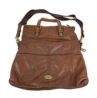 Front view of the large brown leather Fossil travel bag showing its handles, front zipper pocket, and logo plaque. The leather shows wear and some stains.