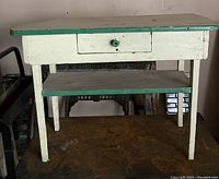 Front view of the antique cream and green painted solid wood table showing drawer and lower shelf.