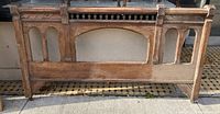 Full view of antique solid wood bed footboard showing overall shape and carved design details.