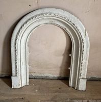 Front view of white painted cast metal fireplace arch insert section leaning against wall