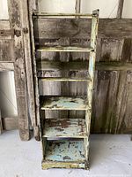 Front view of green painted wooden shelf unit with five shelves, showing worn paint and distressed finish.