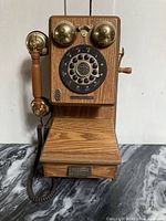 Front full view of the Thomas wood wall telephone showing wooden body, rotary dial, brass bells, and handset.