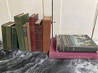 12 vintage hardcover books arranged standing and lying on surface showing covers and spines.