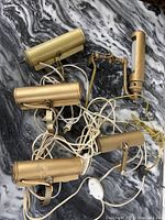 Five vintage gold-tone metal picture lights with cords and plugs on a marble-patterned surface.