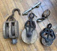 Five antique block and tackle pulleys arranged on wooden floor showing variety of sizes and styles.