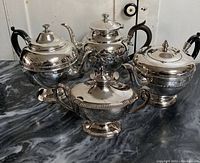 Four silver plate tea/water pots and sugar bowl displayed on a black marble surface, showing overall condition and design