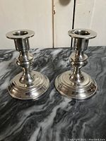 Pair of pewter candle holders standing on a black and white marbled surface with a white door background.