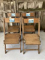Set of four wooden folding chairs arranged in two rows, showing front view with visible blue and white scenic ceramic tiles on backrests.