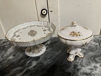 Both vintage decorative dishes side by side on marble surface, showing white porcelain and bone china with gold floral patterns
