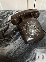 Front angle view of the brown rotary telephone placed on a marble surface