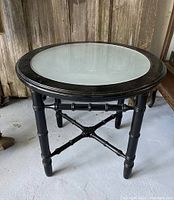 Full view of the vintage round side table with faux bamboo style black painted wooden frame and clear glass top.