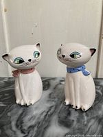 Front view of the pair of vintage Holt Howard cat salt and pepper shakers on a marble surface, showing facial and scarf details.