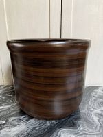 Front view of large brown pot with horizontal banding and flared rim shown against white wooden backdrop.
