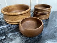 Five vintage teak bowls displayed on black marble surface, showing varying shapes and sizes with visible wood grain and mid-century modern design
