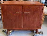Front exterior view of teak cabinet with two doors, recessed handles, tapered legs
