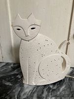 Front and side view of cream-colored ceramic cat lamp with star-pattern perforations and stylized facial features.