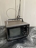 Full view of vintage Sony Trinitron portable television showing front face with screen, controls, handle, and antenna.