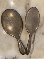 Two vintage sterling silver hairbrush and hand mirror laid flat on a marble surface showing overall shape and monogram engravings.