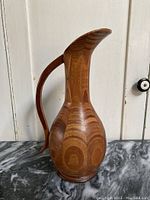 Side view of vintage wooden segmented pitcher showing carved handle and wood grain pattern.