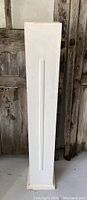 Front view of tall white painted wooden pedestal with decorative vertical grooves
