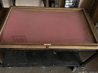 Top view of the wood framed glass tabletop display case with red base and metal latch hardware visible.
