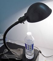 Side view of the desk lamp illuminated, showing the lamp's dome shade and flexible gooseneck attached to a decorative Gothic style base with carved details.