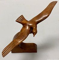 Front view of wooden bird figure in flight, showing detailed carving and smooth polished wood finish on the wings, head and tail.