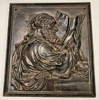 Front view of rectangular cast iron plaque depicting a philosopher or scribe reading a large book, showing details of the figure and original patina.