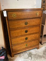 Front view showing five drawers with brass colored pulls and visible wood grain finish. Scratches and signs of wear on drawer fronts.