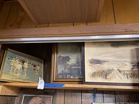 Three framed paintings on a shelf, showing different earth and muted tones artwork.