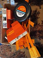 Cardboard box containing assorted orange Hot Wheels track pieces and two toy building structures