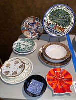 Top view of the lot showing multiple decorative plates including Imari style and Quimper style plates, a serving bowl, and an ashtray
