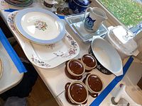 Wide photo showing platters, plates, corningware bakeware with lid, ceramic owl pitcher and four small brown lidded soup bowls