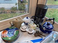 View of the lot showing several teapots, a Braun coffee maker, colorful ceramic Sango plates, and cream and sugar set.