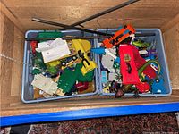 Overhead view of two blue crates containing mixed plastic vehicles, base plates, accessories and plush toys