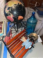 Image showing vintage globe, black metal decorative bike, blue covered glass jar, small wooden doll bench with figurine and American flag, and metal bowl.
