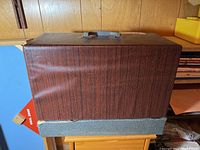 Outside of sewing machine case showing faux wood contact paper covering with plastic handle on top.