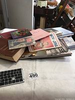 Top view of a stack of books and magazines on a white tablecloth, showing various titles and covers.