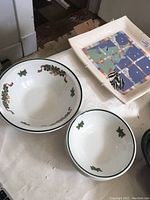 Two white ceramic Christmas bowls with green trim and holly decorations, alongside a square abstract patterned platter.