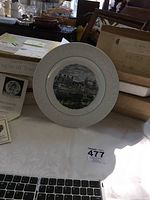 Tower of London collector plate on white cloth with original paperwork beside it. Plate has embossed floral design on rim and central image of Tower of London in color.