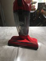 Front view showing full upright Dirt Devil Vibe stick vacuum with red housing and transparent dust compartment.