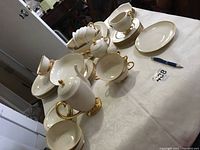 Photo of the entire Flintridge China dinnerware set, arranged on a table, showing gold-trimmed white china pieces including cups, saucers, plates, serving bowls, teapot, sugar bowl, creamer, and salt & pepper shakers.